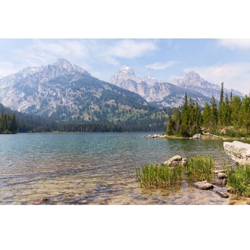 Mountain lake with clear water and Teton mountains behind the lake 