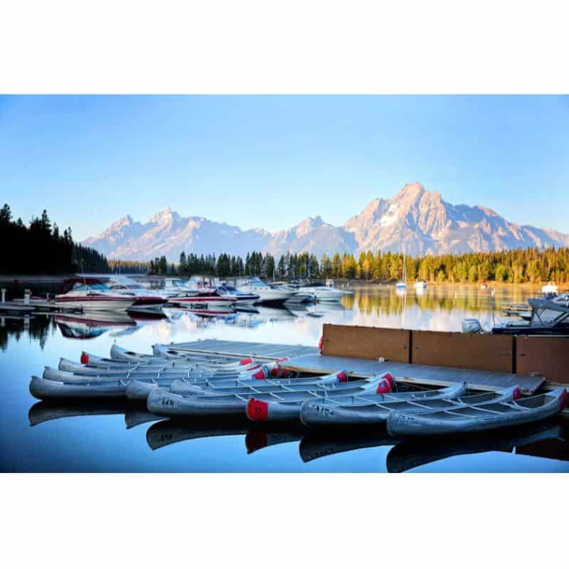 kayaks and row boats on a lake with pine trees and mountains 