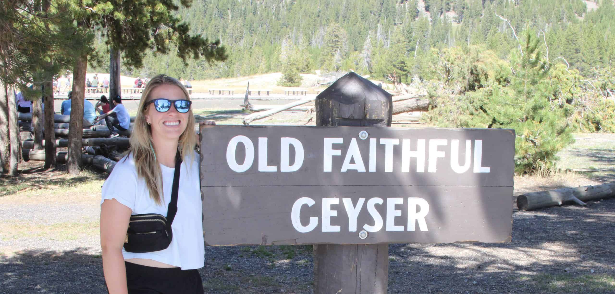 Woman near sign for the Old Faithful in Yellowstone National Park 