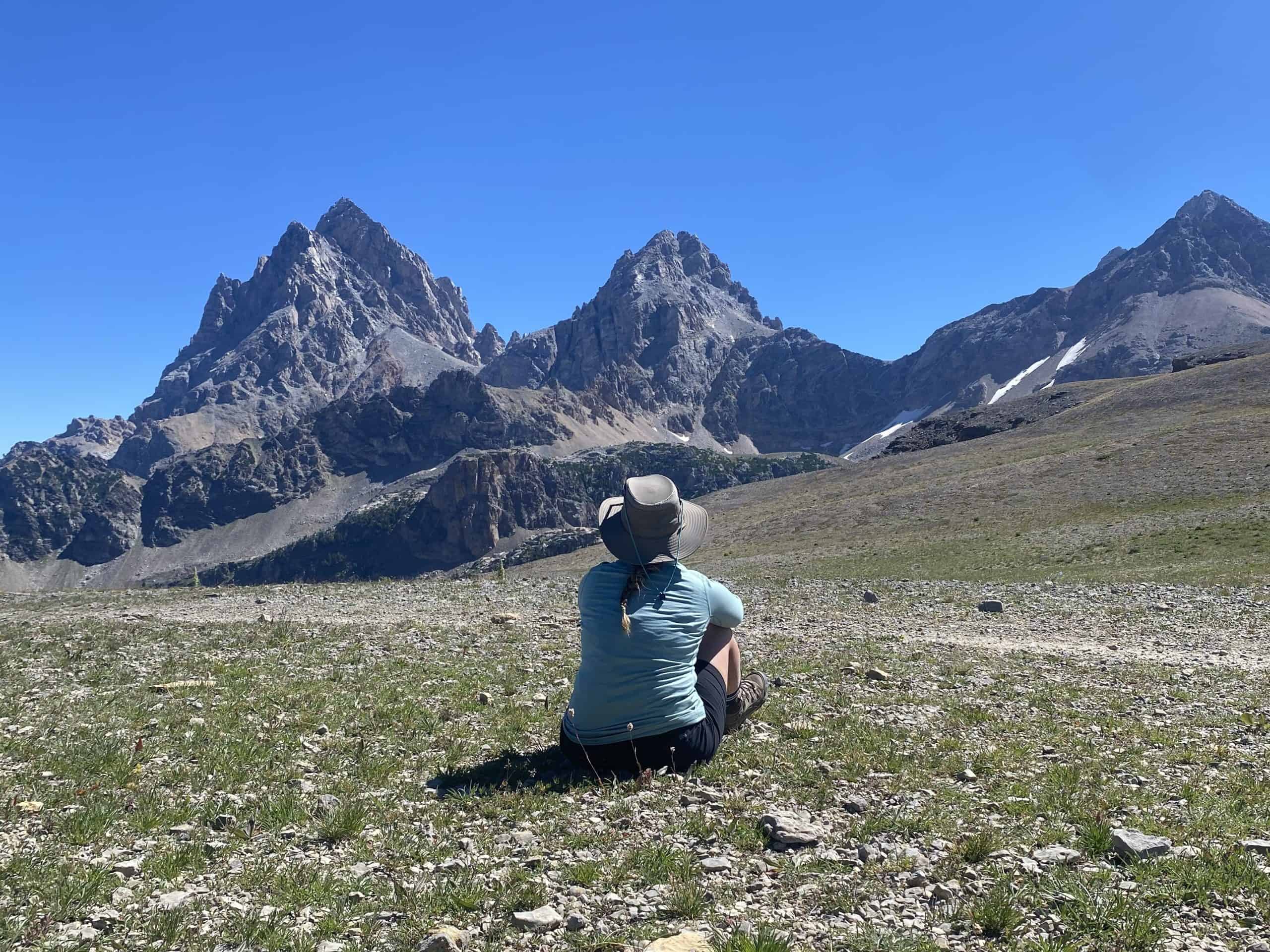 Woman sitting on the ground looking at the Grand Teton mountains