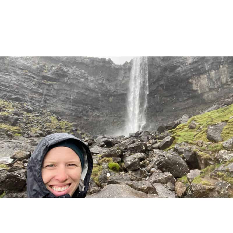 Woman standing in rain with waterfall and black cliff in background