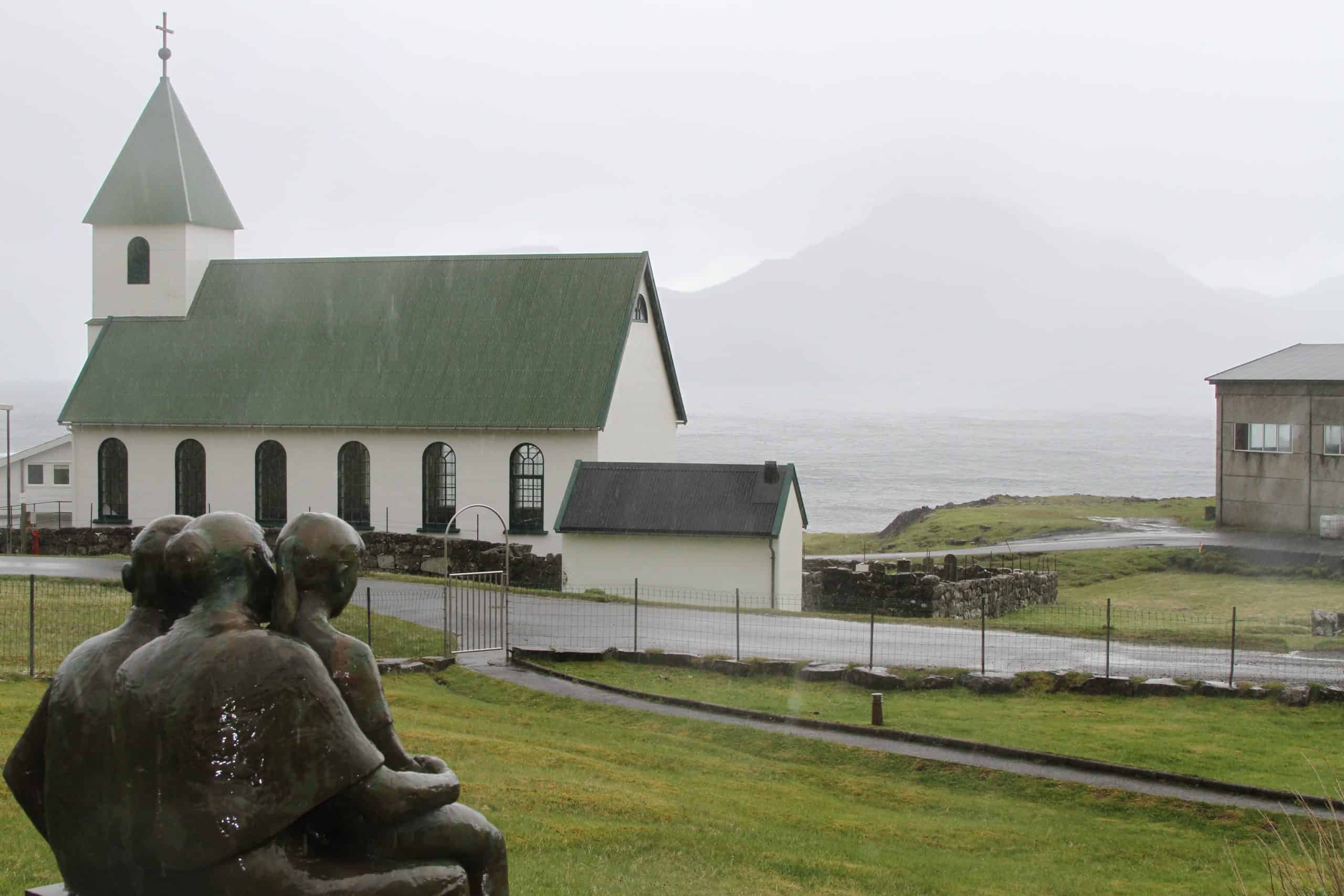 Statue of woman with children and a white church in the background in the rain 