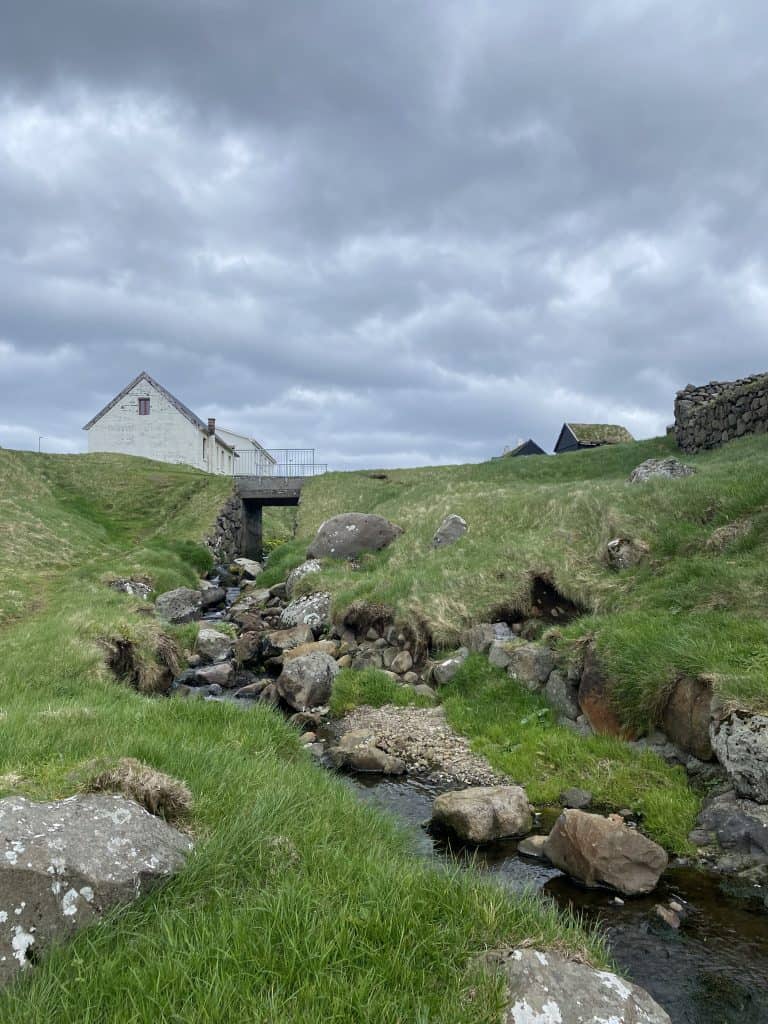 Creek with rocks and grass, bridge and homes nearby