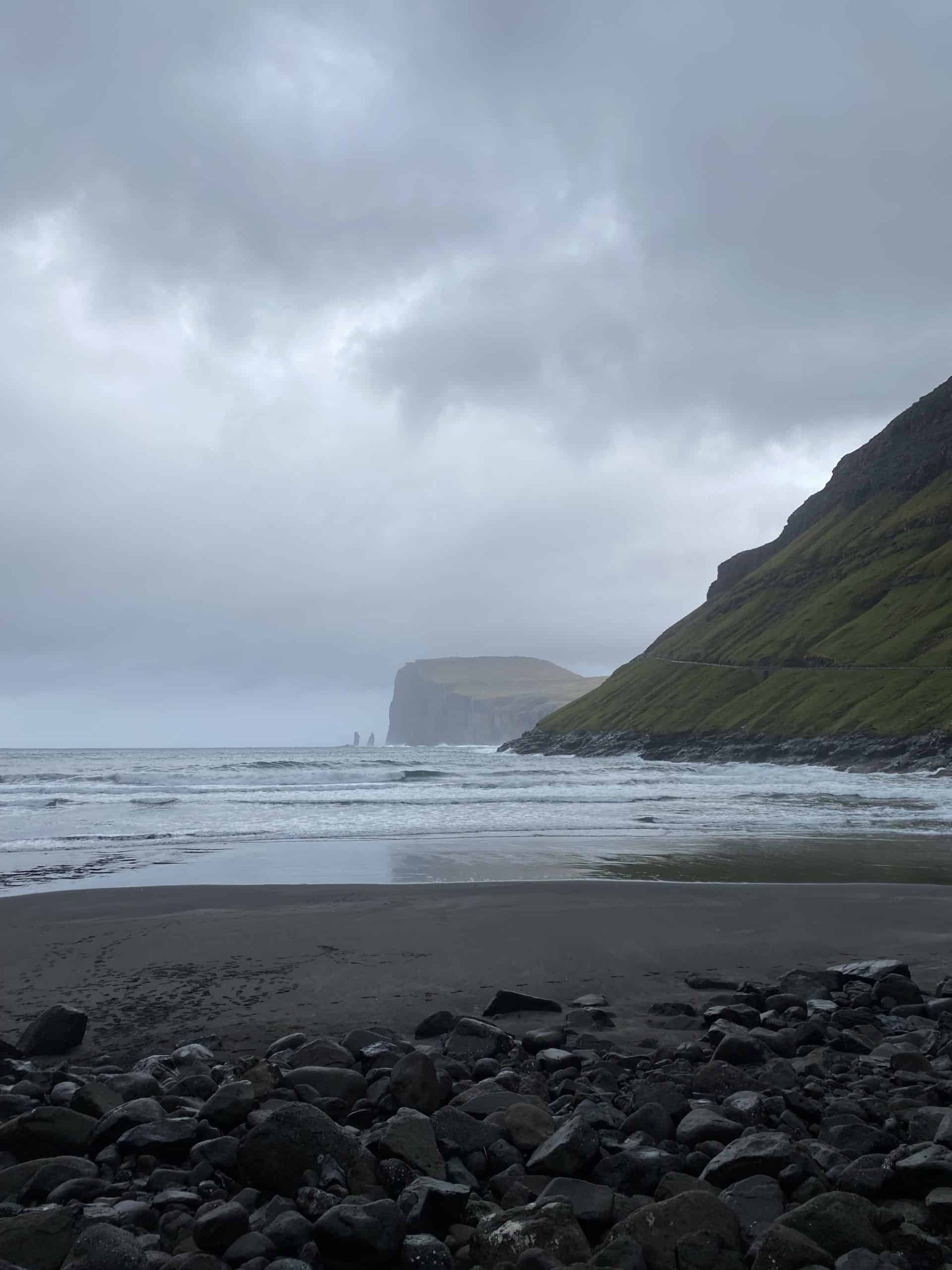 Black sand beach with grey skies and green mountains