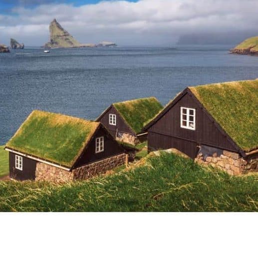 Cabins with grass roofs on the side of a cliff with ocean and islands on horizon