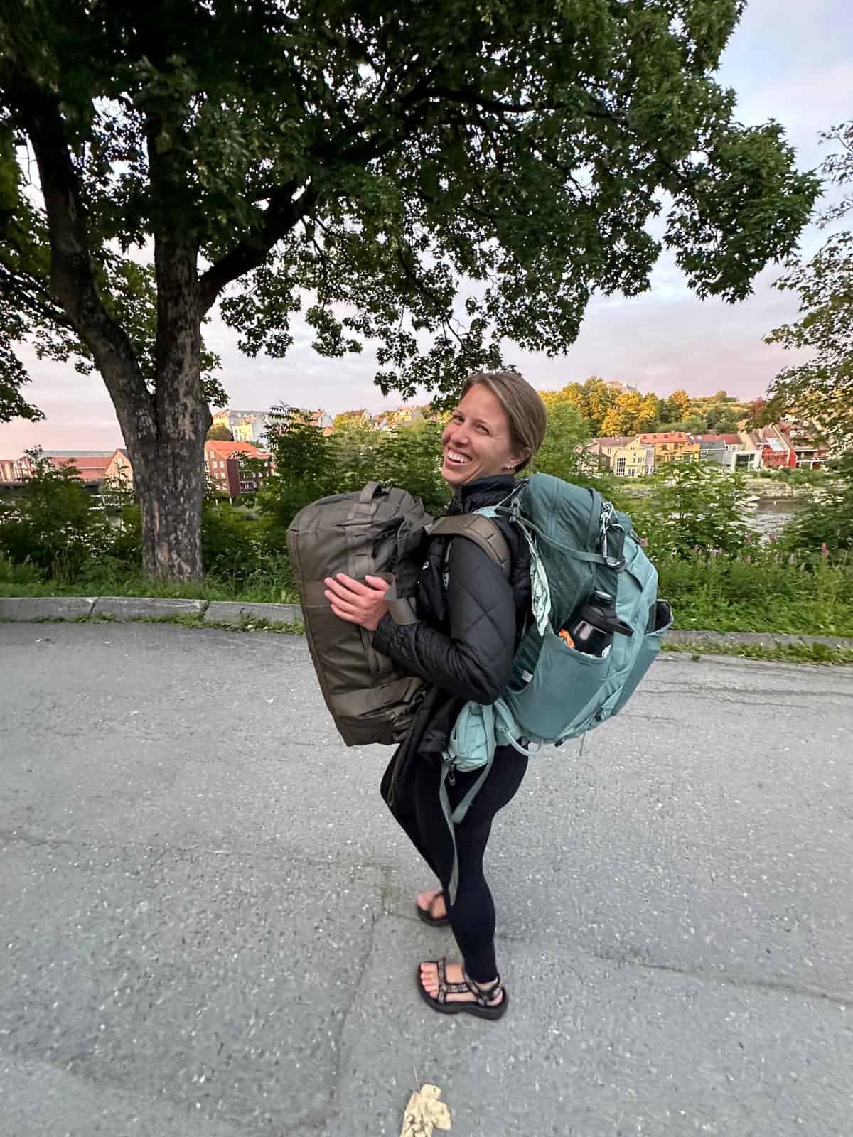 Woman carrying two backpacks walking through Trondheim. 