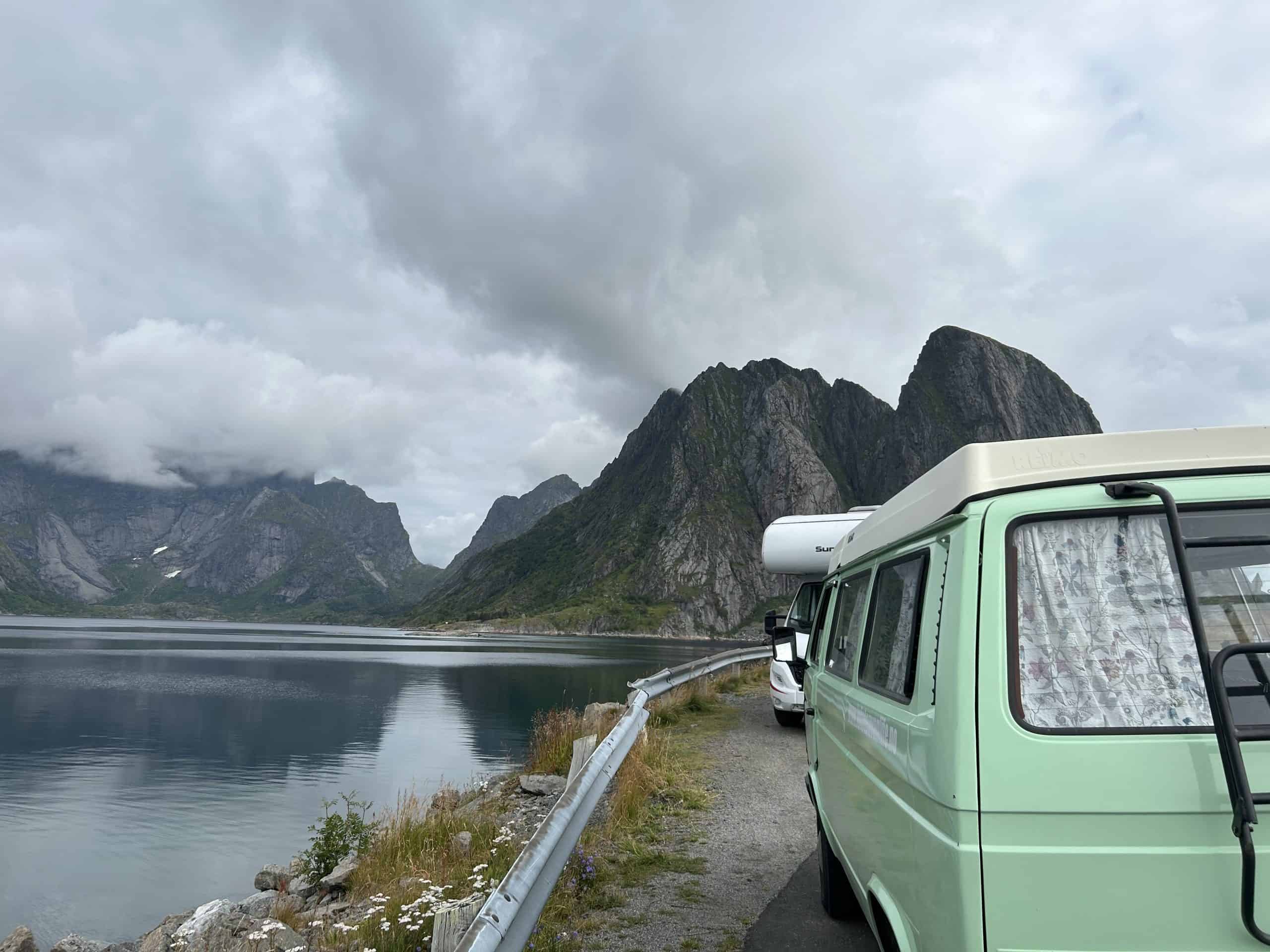 Mint green Volkswagen van with other RV in background and mountains and fjord. 