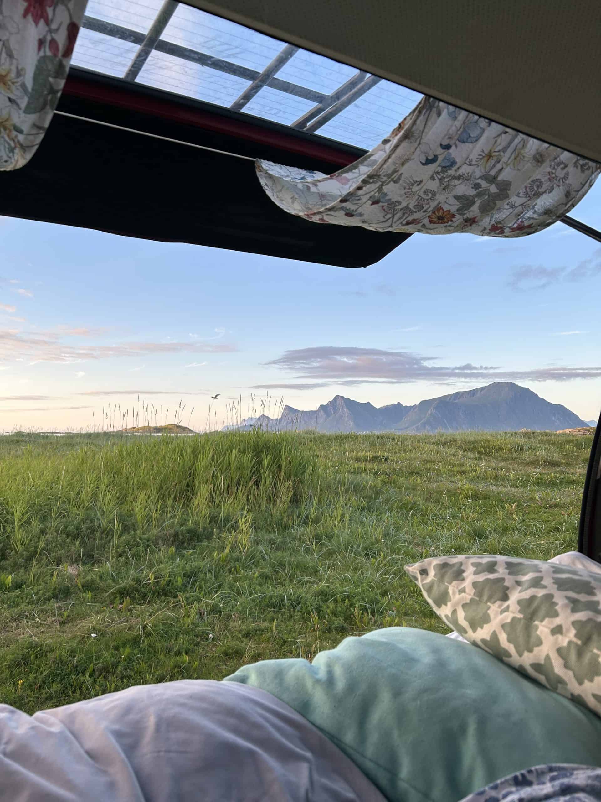 Hatch of Volkswagen van open with pillows and mountains in the background at sunset. 