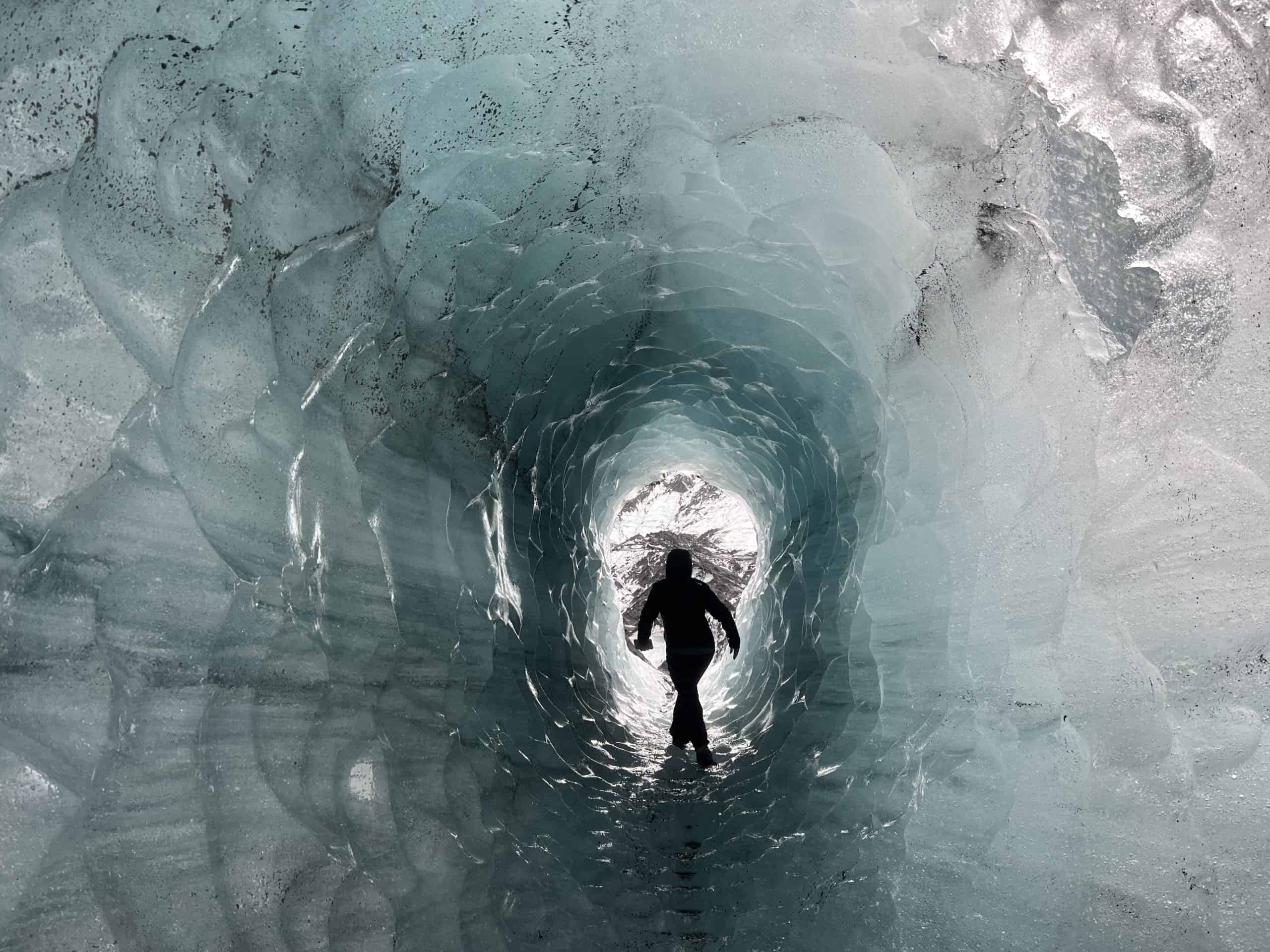 Woman hiking through ice cave with light blue coloring. 