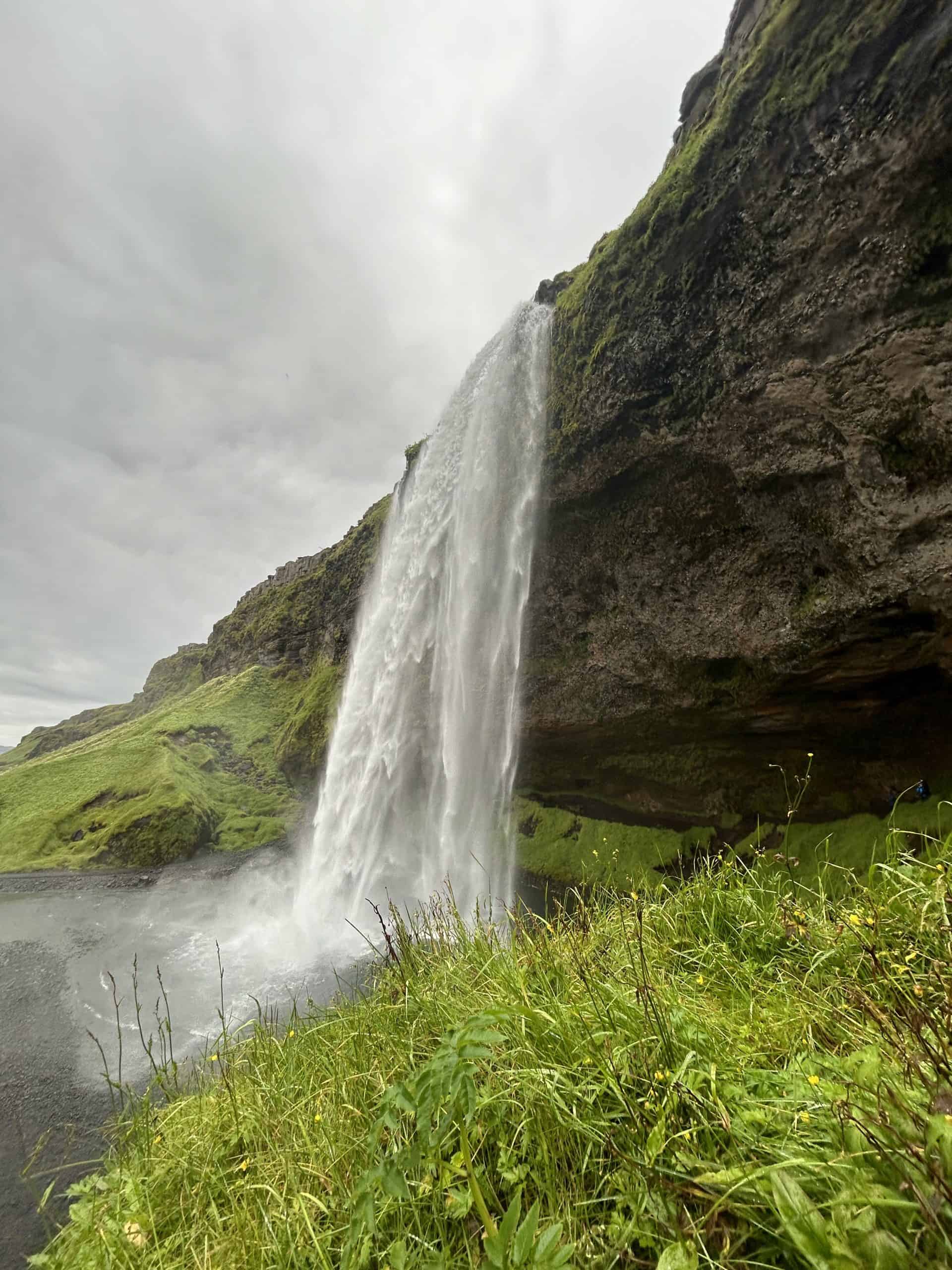 Waterfall with green grass and mountains in. 